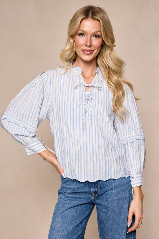 A woman with long blonde hair models the Ivy City Co Leticia Top in White & Blue Stripe, styled with blue jeans against a beige background—a cheerful, on-trend choice for your spring wardrobe.