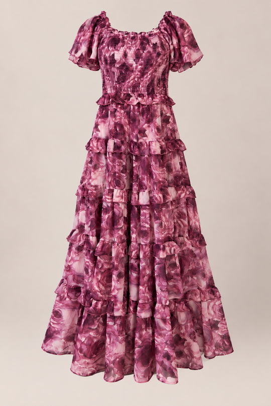 The Winnie Dress in Dreamy Roses by Ivy City Co is a long, ruffled chiffon girls’ dress featuring short sleeves, a fitted bodice, and a tiered skirt. Showcasing a mauve and pink floral pattern accented with a subtle gold metallic stripe, this charming holiday dress is displayed against a neutral background.