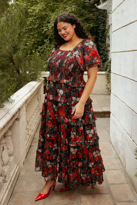 Woman in a floral dress standing outdoors on a stone path with greenery.