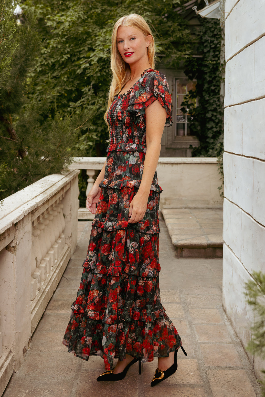 Woman in a floral dress standing on a stone pathway with greenery in the background