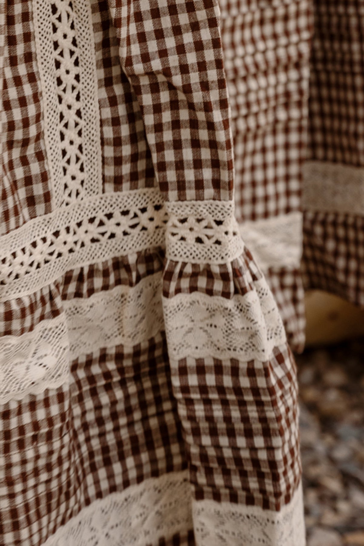 Close-up of brown and white hickory gingham fabric with intricate white lace details, showcasing the various patterns and textures from the Ivy City Co Mini Palermo Dress in Hickory Gingham—a charming cotton-blend dress for girls. The background is slightly out of focus.