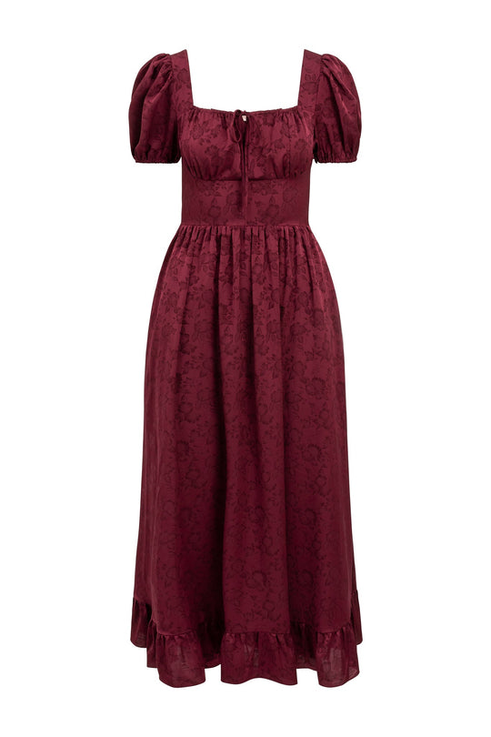 The Amira Dress in Red by Ivy City Co features elegant puff sleeves, a square neckline, and a fitted bodice with a charming tie detail at the chest. Made from jacquard fabric with a subtle woven floral pattern, this midi dress is finished with a gathered waist and ruffled hem for added sophistication.
