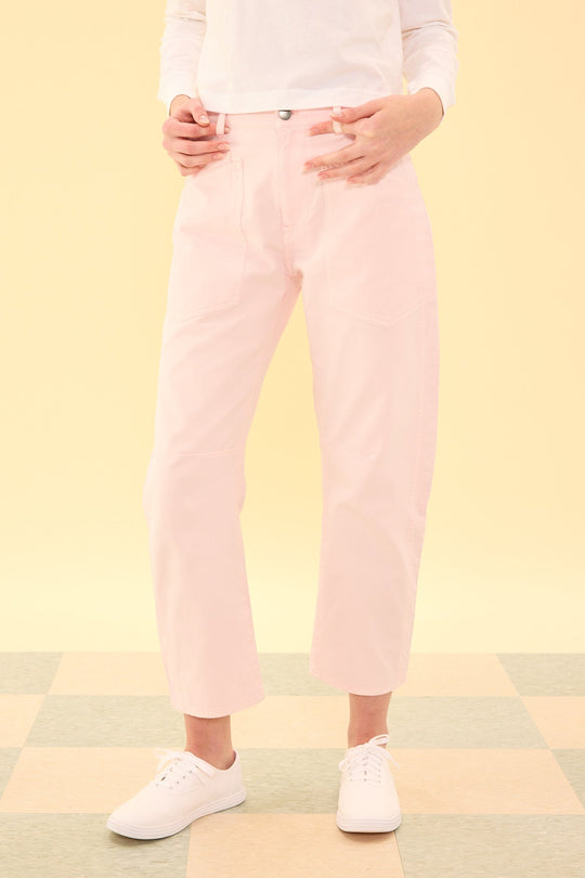 A person wearing the Amanda Pants in Light Pink by Ivy City Co, paired with a white long-sleeve shirt and white sneakers, stands on a checkered floor against a pale yellow background.