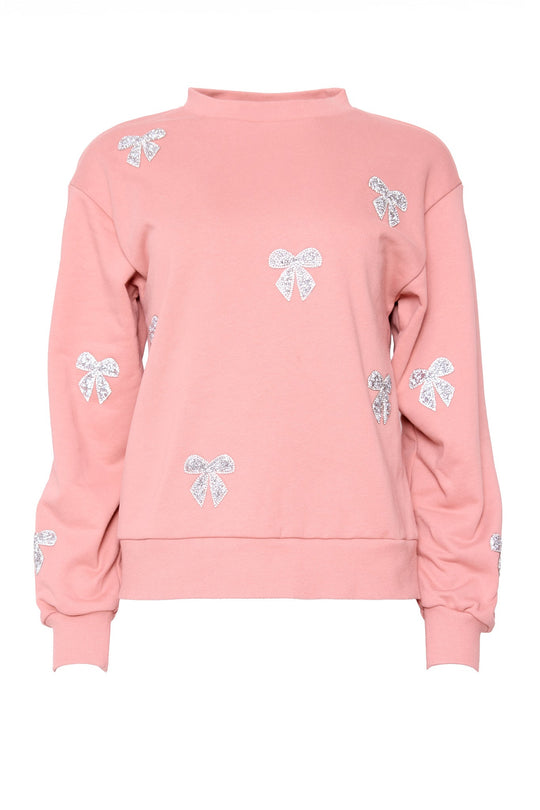 The Micah Crew Neck Sweatshirt in Pink & Bows by Ivy City Co features a pink base adorned with multiple white glittery bow designs scattered across the front and sleeves, making it a sparkling addition to your Ivy City Co Lounge Collection.