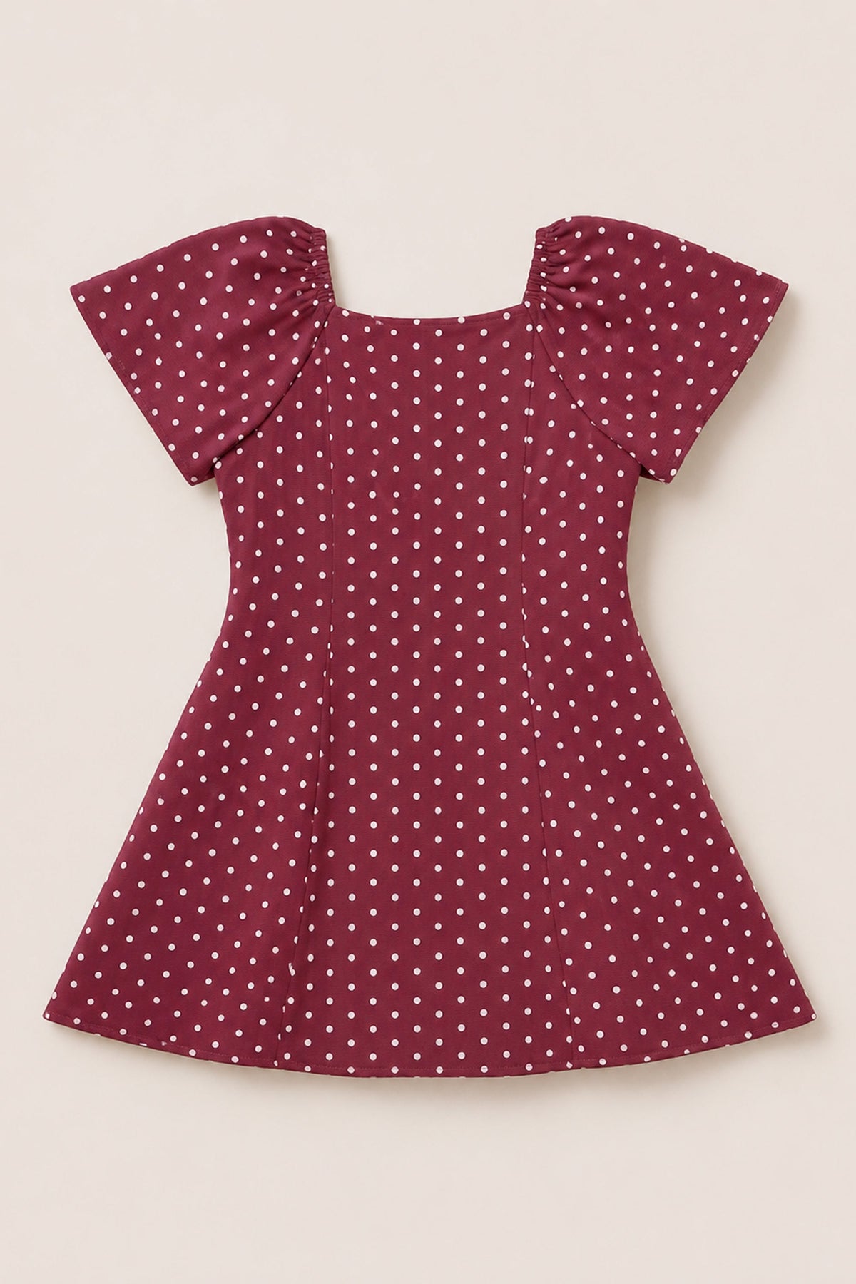 A Teen Blakely Dress in Cranberry Dainty Dot by Ivy City Co, featuring short puffed petal sleeves, white polka dots, and a flared midi-length skirt, is laid flat on a neutral background.