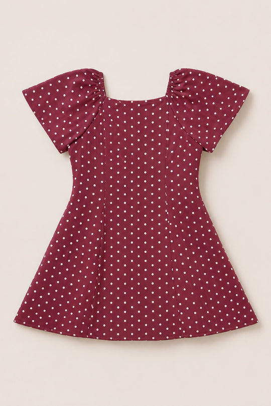 A Teen Blakely Dress in Cranberry Dainty Dot by Ivy City Co, featuring short puffed petal sleeves, white polka dots, and a flared midi-length skirt, is laid flat on a neutral background.