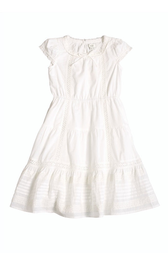 The Mini Palermo Dress in White by Ivy City Co features short sleeves, a knee-length cotton silhouette with lace details, a smocked bodice, round neckline, and ruffled hem, shown laid flat on a white background.