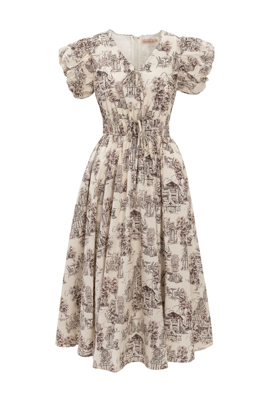 The Zaza Midi Dress in Brown Toile by Ivy City Co features a cream cotton midi silhouette with puffed short sleeves, a fitted waist, and a vintage-inspired brown toile print depicting pastoral scenes.