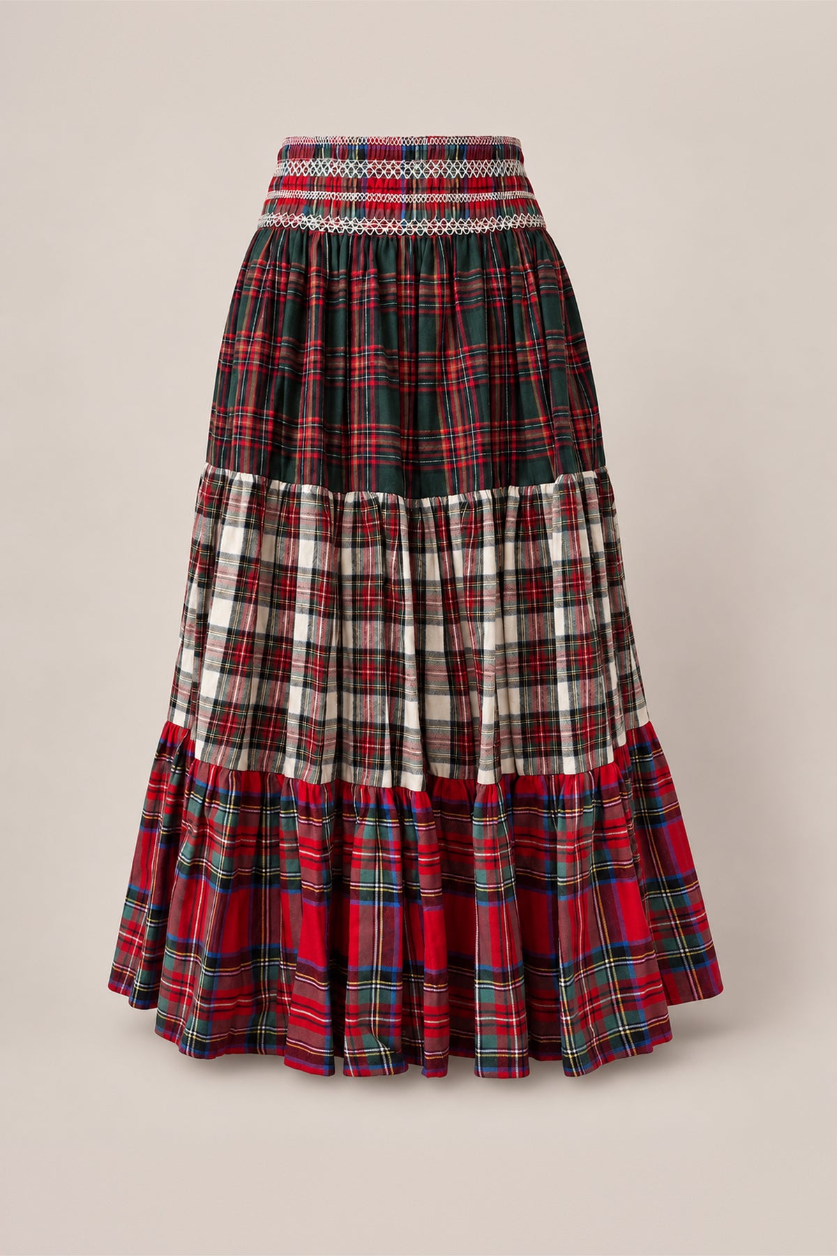 The Zoey Skirt in Mixed Plaid by Ivy City Co features a long, tiered cotton A-line silhouette with a smocked waistband for comfort, designed with a patchwork of red, green, and white plaid patterns. Displayed against a plain beige background, this holiday family skirt is also maternity friendly, making it perfect for special occasions.