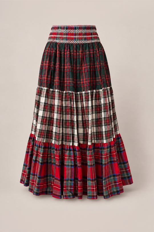 The Zoey Skirt in Mixed Plaid by Ivy City Co features a long, tiered cotton A-line silhouette with a smocked waistband for comfort, designed with a patchwork of red, green, and white plaid patterns. Displayed against a plain beige background, this holiday family skirt is also maternity friendly, making it perfect for special occasions.