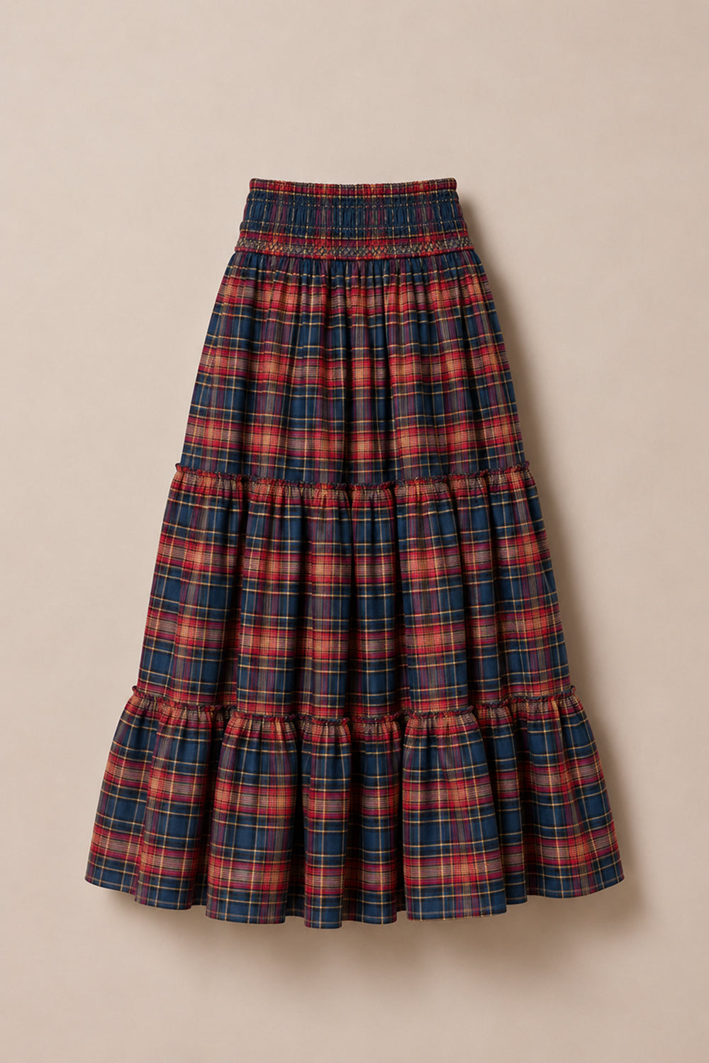 The Zoey Skirt in Twilight Plaid by Ivy City Co is a long, tiered cotton A-line skirt featuring a smocked waistband and a vibrant red, blue, and yellow plaid pattern, shown laid flat on a beige background—ideal for effortless fall style.
