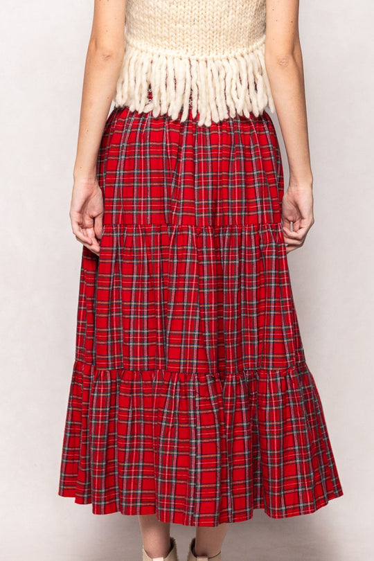 Woman wearing a white sleeveless top with fringe and a red plaid skirt on a white background