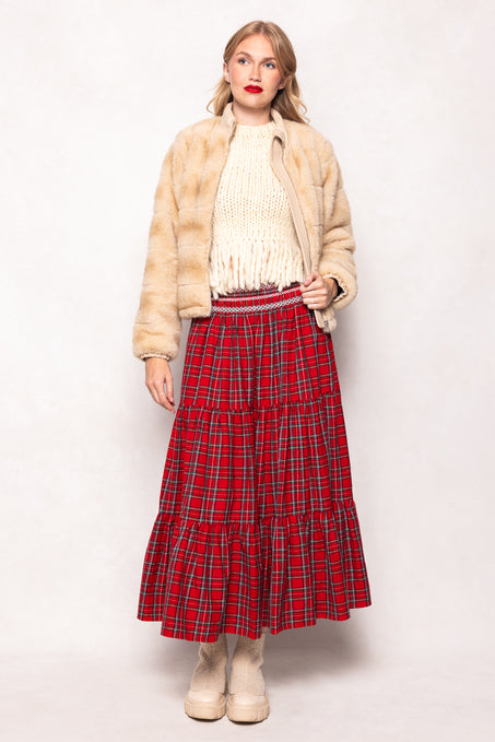 Woman wearing a red plaid skirt, beige jacket, and white sweater on a white background