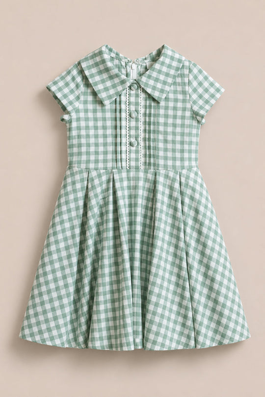 The Mini Amber Dress in Sage Gingham by Ivy City Co features a Peter Pan collar, button details, and a pleated skirt. This charming cotton midi dress is displayed laid flat on a neutral background.