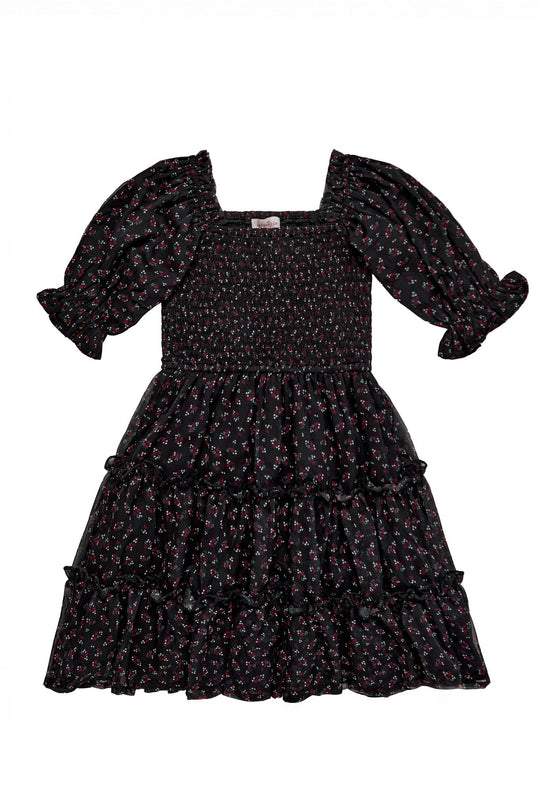 The Mini Madeline Dress in Black Ditsy Floral by Ivy City Co features puff sleeves, a smocked bodice, and a square neckline with a tiered ruffle skirt. This charming mini dress is crafted from black fabric adorned with a subtle red and white ditsy floral print for an effortlessly feminine look.