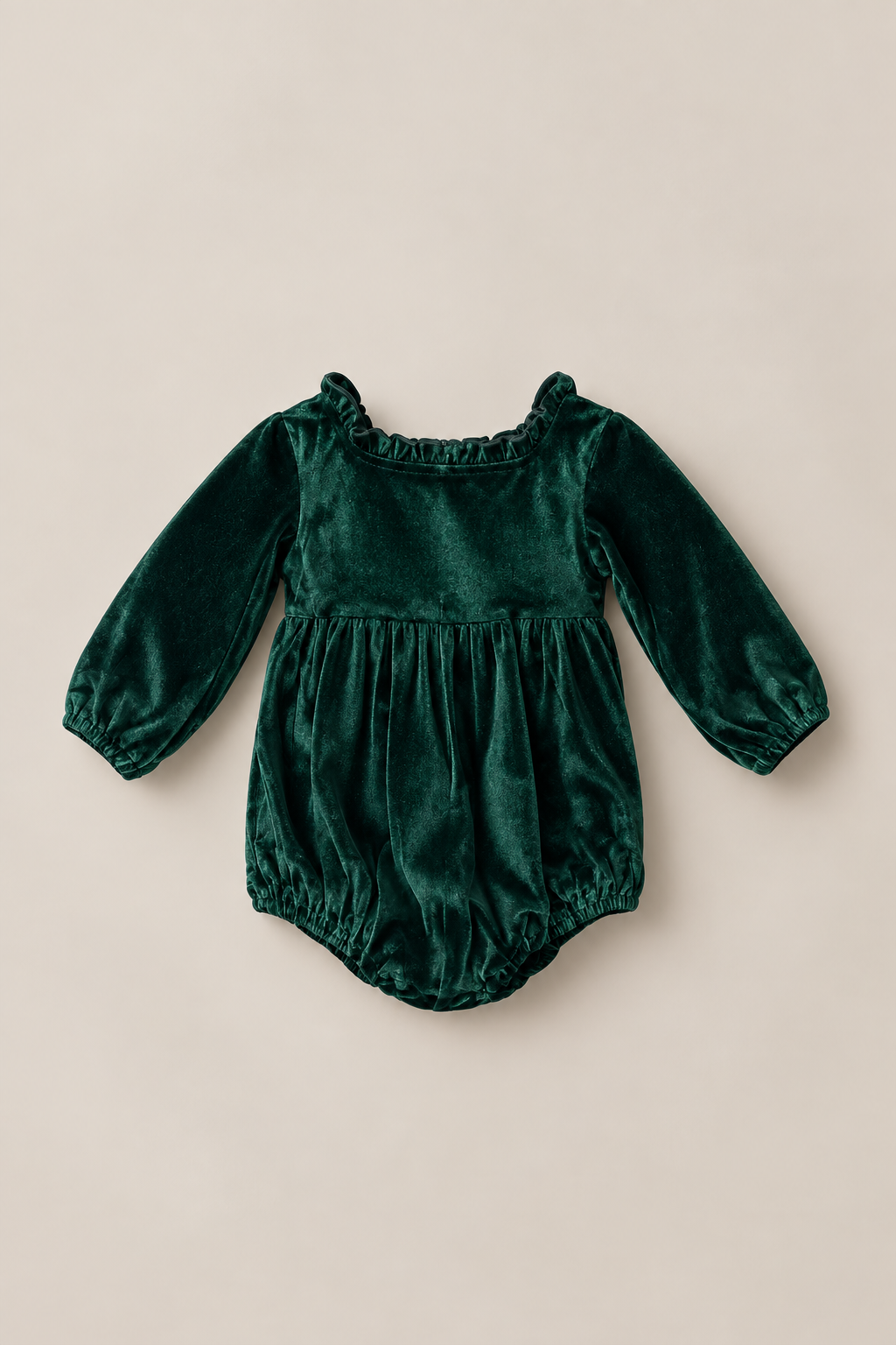 The Ivy City Co Baby Cypress Romper in Green Velvet features long sleeves, delicate ruffle detailing at the neckline, a gathered waist, and elastic leg openings, shown against a light beige background.
