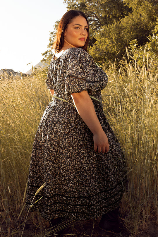 Woman in a floral dress standing in a field with trees in the background