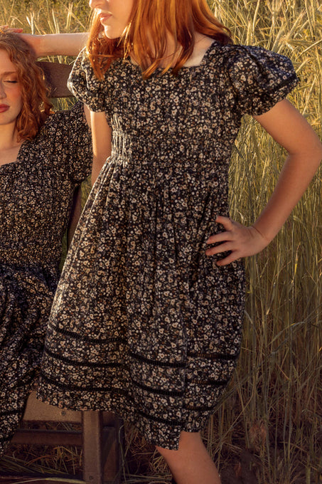 mom and daughter in floral dresses standing in a field.