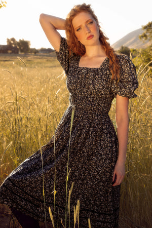 Woman in a floral dress standing in a field with mountains in the background