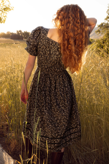 Woman in a floral dress standing in a field of tall grass with a sunset in the background