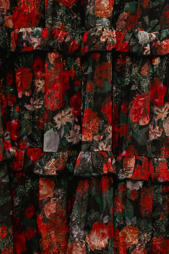 A close-up of the Winnie Dress in Midnight Roses by Ivy City Co reveals fabric with a ruffled texture, adorned in a floral pattern of red, green, and black hues. Featuring prominent roses and leafy accents reminiscent of the signature Midnight Roses motif, this richly textured and layered design exudes elegance while offering a maternity-friendly fit.