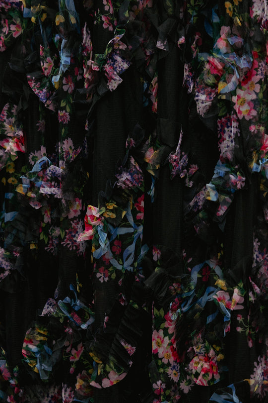 Close-up of the Florentina Dress in Obsidian Garden by Ivy City Co—a black tulle evening dress adorned with vibrant pink, yellow, and blue floral patterns. This maternity-friendly design features elegant ruffled layers and textured details for a striking yet comfortable look.