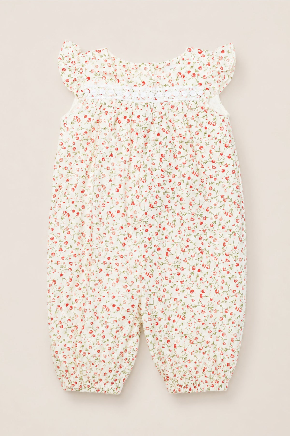The Ivy City Co Baby Mirabelle Romper in Cream Ditsy Floral is crafted from soft cotton and features flutter sleeves, a charming red and green ditsy floral print on a white background, smocked detailing at the chest, and delicate elasticized ankle cuffs—combining comfort and style for your little one.