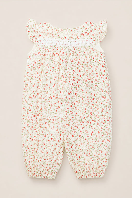 The Ivy City Co Baby Mirabelle Romper in Cream Ditsy Floral is crafted from soft cotton and features flutter sleeves, a charming red and green ditsy floral print on a white background, smocked detailing at the chest, and delicate elasticized ankle cuffs—combining comfort and style for your little one.