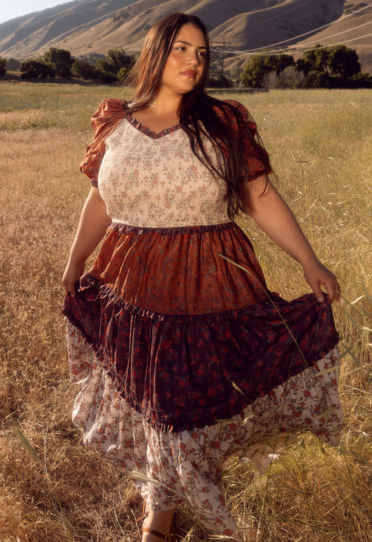 Woman in a vintage dress standing in a field with mountains in the background