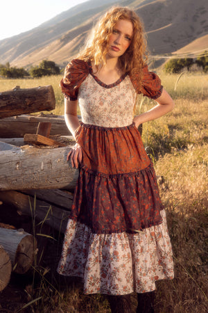 Woman in a historical dress standing in a field with mountains in the background