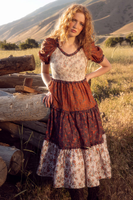 Woman in a historical dress standing in a field with mountains in the background