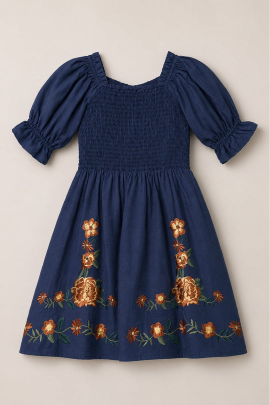 The Mini Teagan Dress in Navy Embroidered Fall Floral by Ivy City Co features a smocked bodice, short balloon sleeves, and orange and gold floral embroidery along the bottom hem.