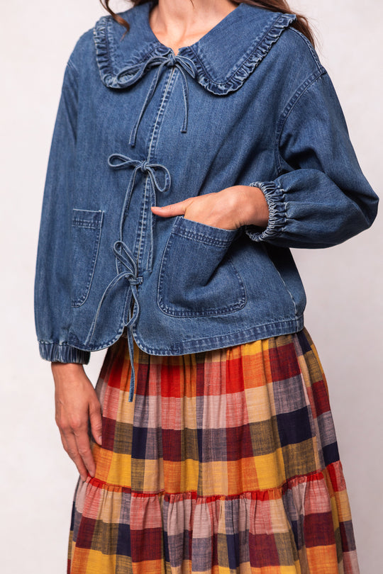 Person wearing a blue denim jacket and plaid skirt on a plain background