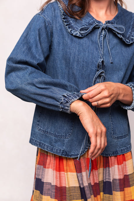 Person wearing a blue denim jacket over a plaid dress on a white background
