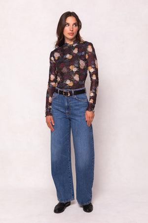 Woman wearing a floral long-sleeve top and blue jeans on a white background