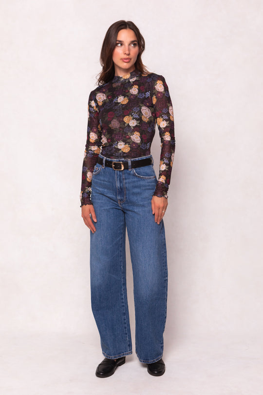 Woman wearing a floral long-sleeve top and blue jeans on a white background