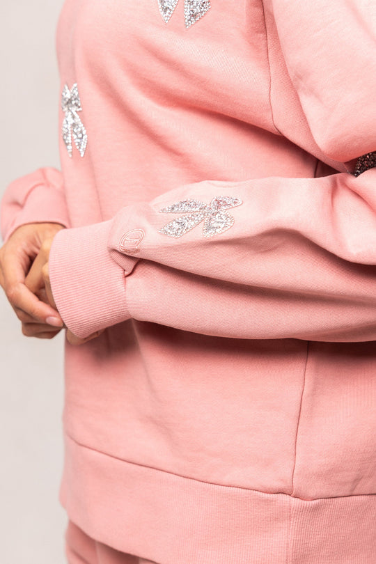 A person is seen wearing the Ivy City Co Micah Crew Neck Sweatshirt in Pink & Bows, with only the side of their torso and one hand visible.