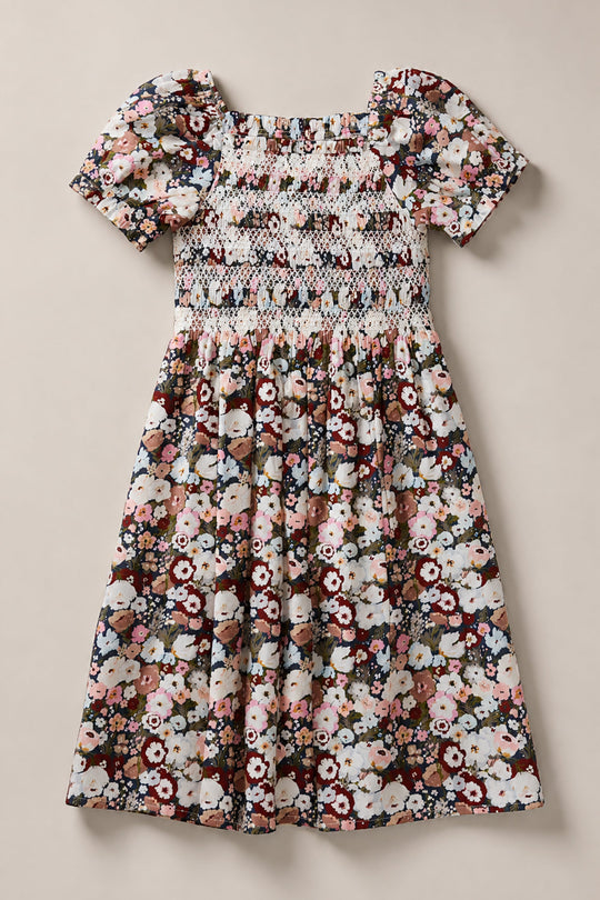 A short-sleeved, knee-length Mini Sunday Best Dress in Midnight Garden by Ivy City Co, featuring a smocked bodice and a colorful floral pattern with pink, burgundy, and green tones on a white background.
