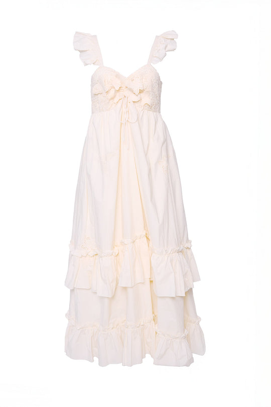 The Gaia Butterfly Dress in Ivory by Ivy City Co features a sleeveless design with ruffled straps, a delicate lace bodice, bow tie at the waist, and a tiered ruffle skirt. Displayed on a plain white background, this dress is perfect for spring portraits and offers a maternity-friendly fit.