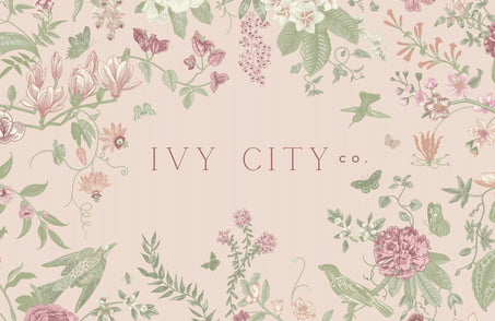 Delicate floral and bird illustrations in soft pastel tones frame “Ivy City Co” on a pale pink background—a charming design for the Ivy City Co Gift Card ($10-$200), available with convenient email delivery.
