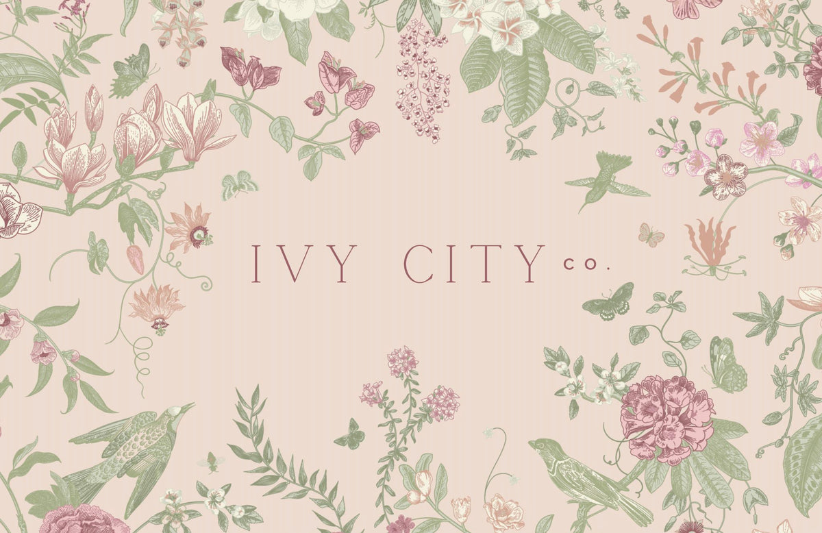 A charming floral illustration featuring birds, butterflies, and assorted flowers encircles the Ivy City Co logo on a pale pink background—making this Gift Card ($10–$250) from Ivy City Co an ideal way to let your loved ones choose their perfect piece in timeless style.