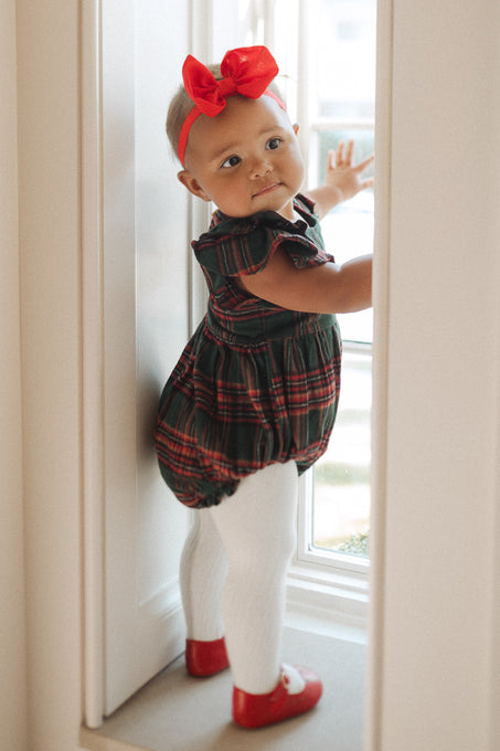 Plaid baby girl romper with ruffled details on sleeve in a window