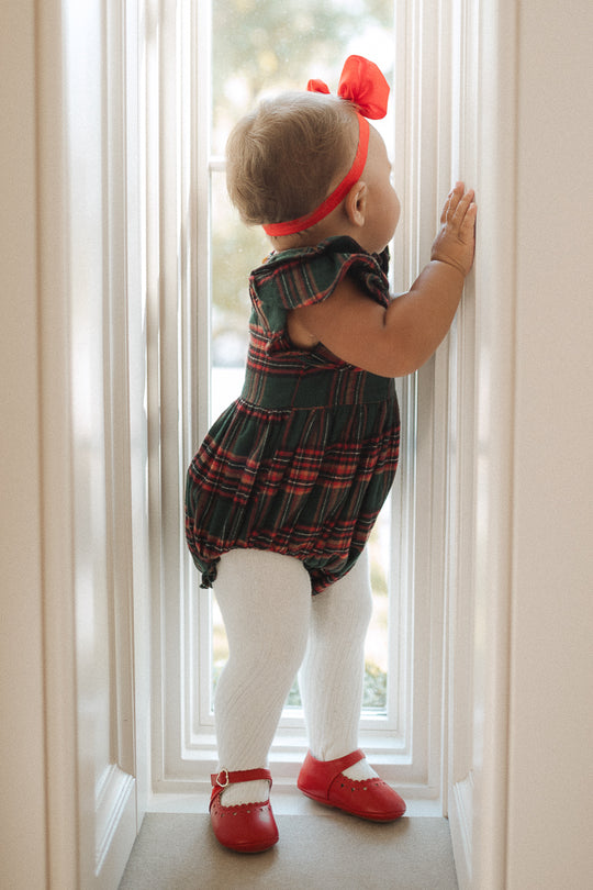 Plaid baby girl romper with ruffled details on sleeve in a window