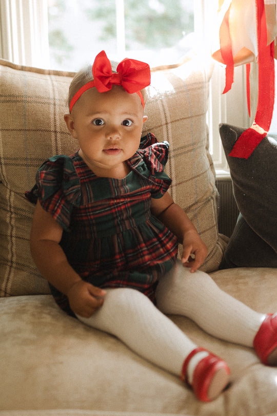 Plaid baby girl romper with ruffled details on sleeve in a window