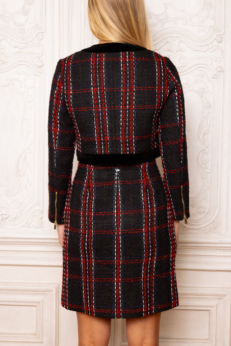 Person wearing a black and red plaid dress against a white wall.