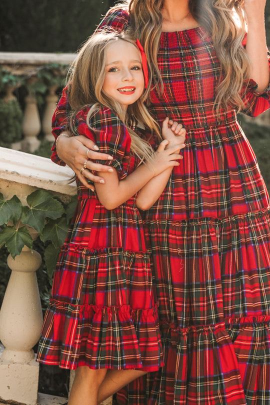 Two people wearing red plaid dresses standing close together outdoors.