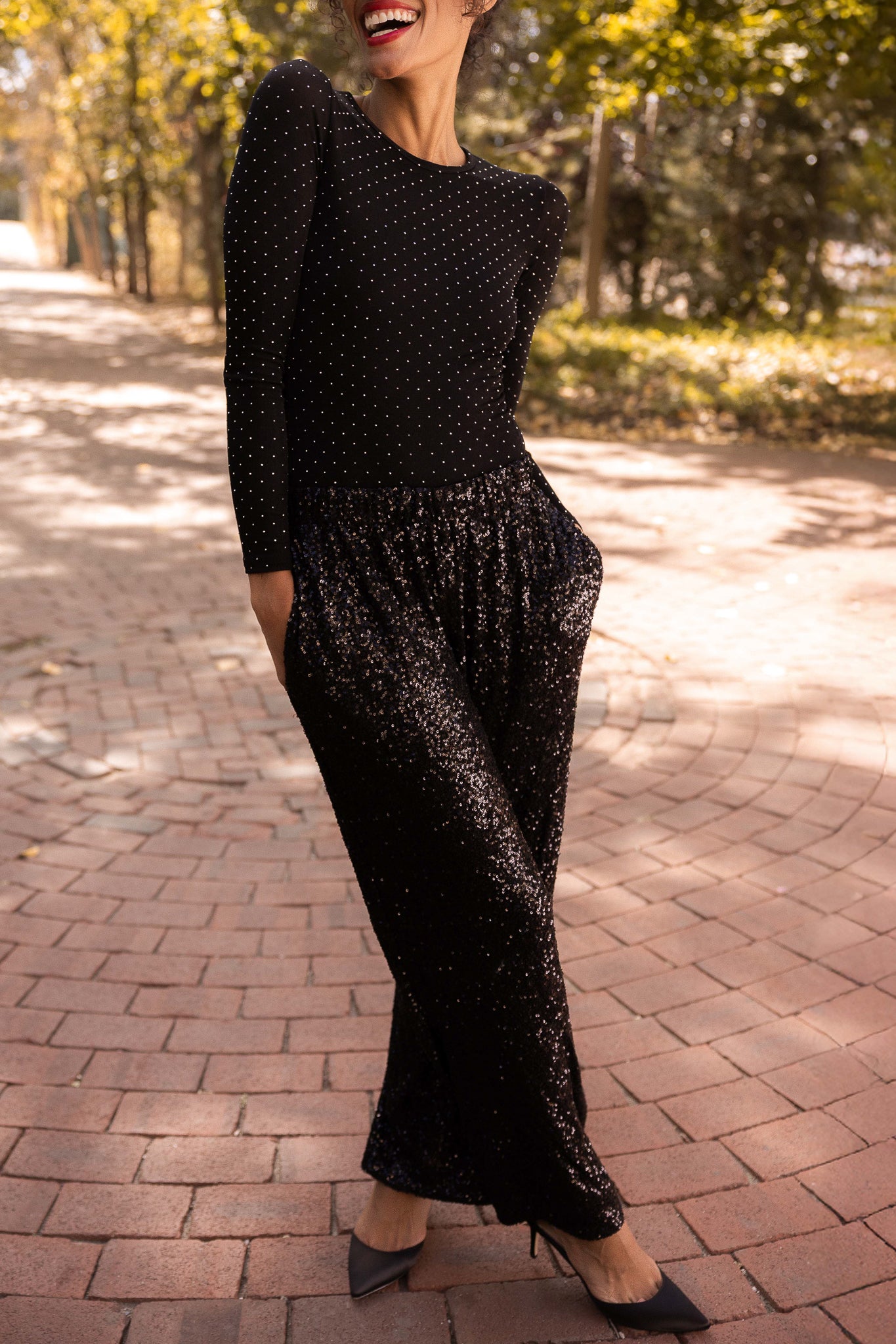 Woman in a black polka dot outfit walking on a brick path with trees in the background