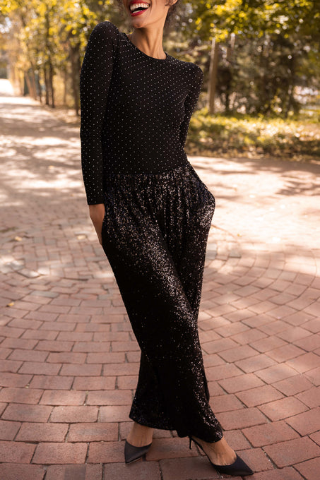 Woman in a black polka dot outfit walking on a brick path with trees in the background