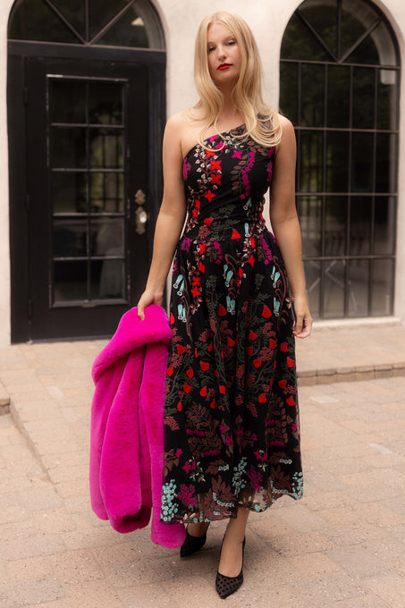 Woman in a floral dress holding a pink fur coat against a building background