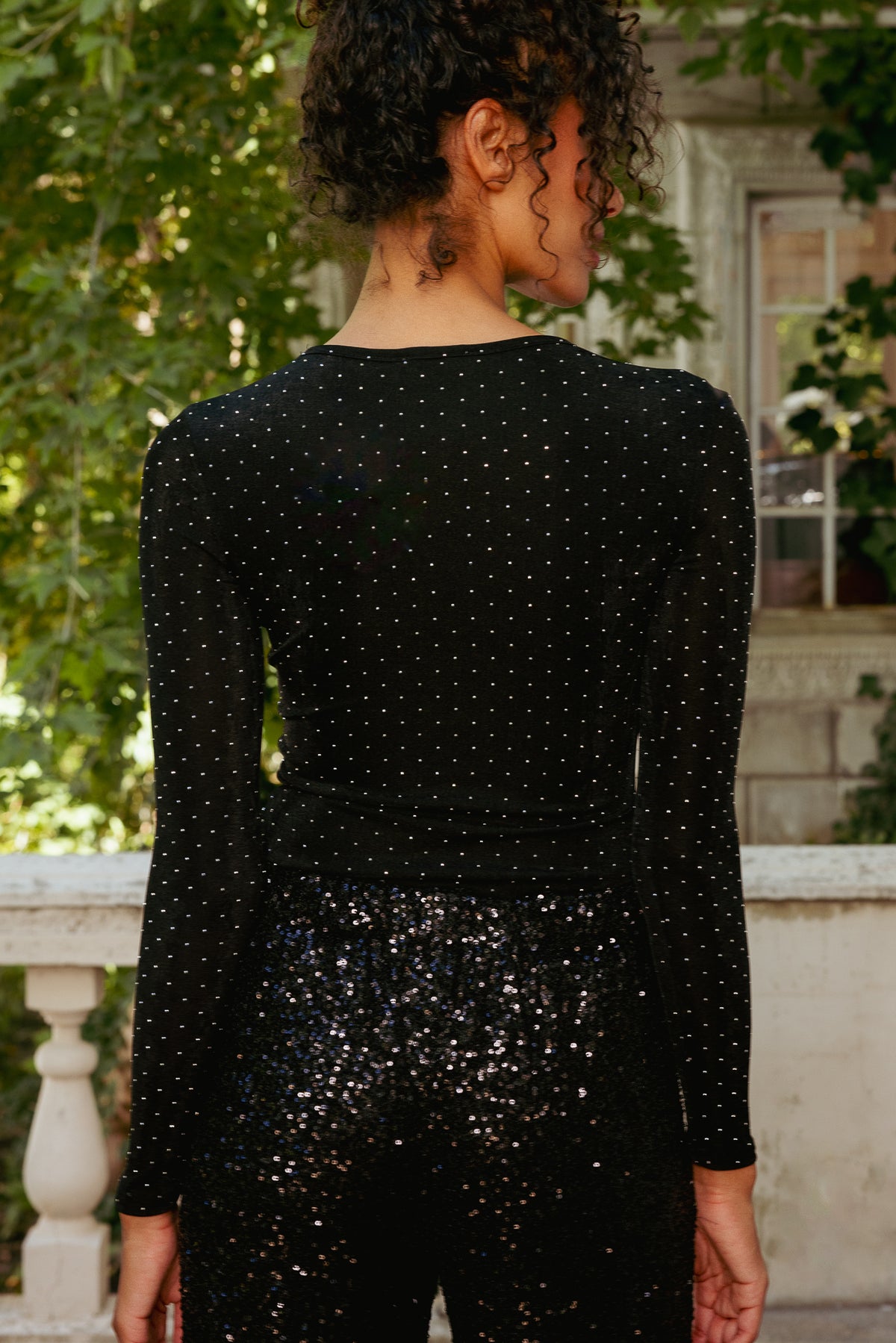 Person wearing a black sequin dress standing outdoors with greenery in the background